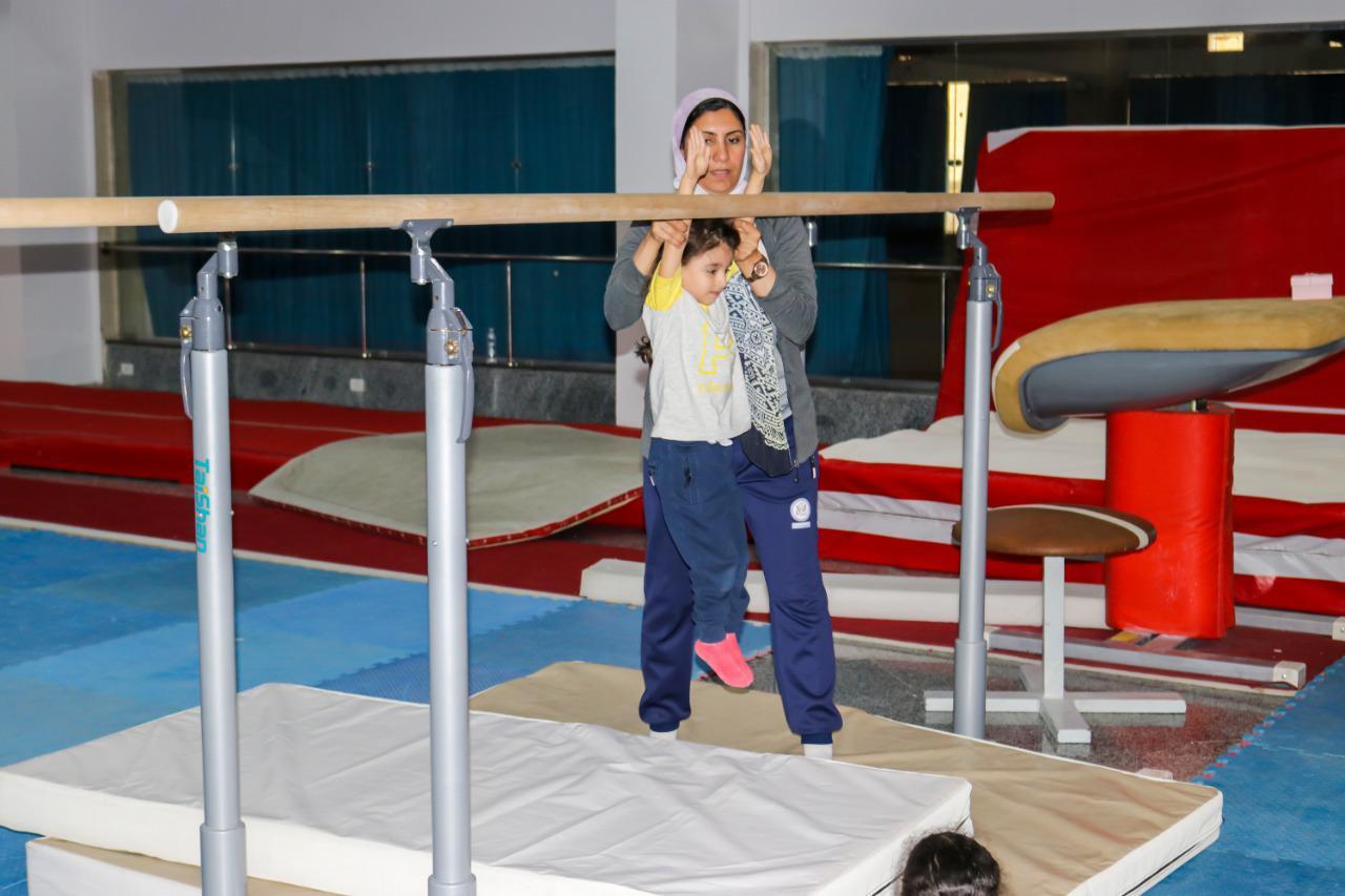 Young child receiving guidance at IVY STEM's gymnastics training facility, surrounded by various gymnastic equipment.