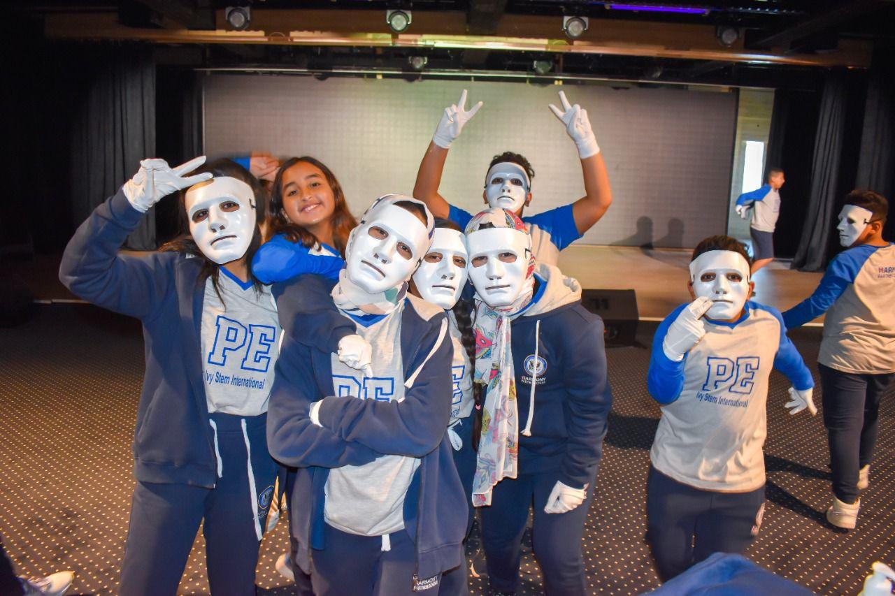 A group of young individuals from IVY STEM International School participating in a physical education activity. They are dressed in matching blue sweatshirts and sweatpants with the letters 'PE' visible. The image showcases their energetic and playful atmosphere, suggesting they are preparing for a performance or celebrating after one.