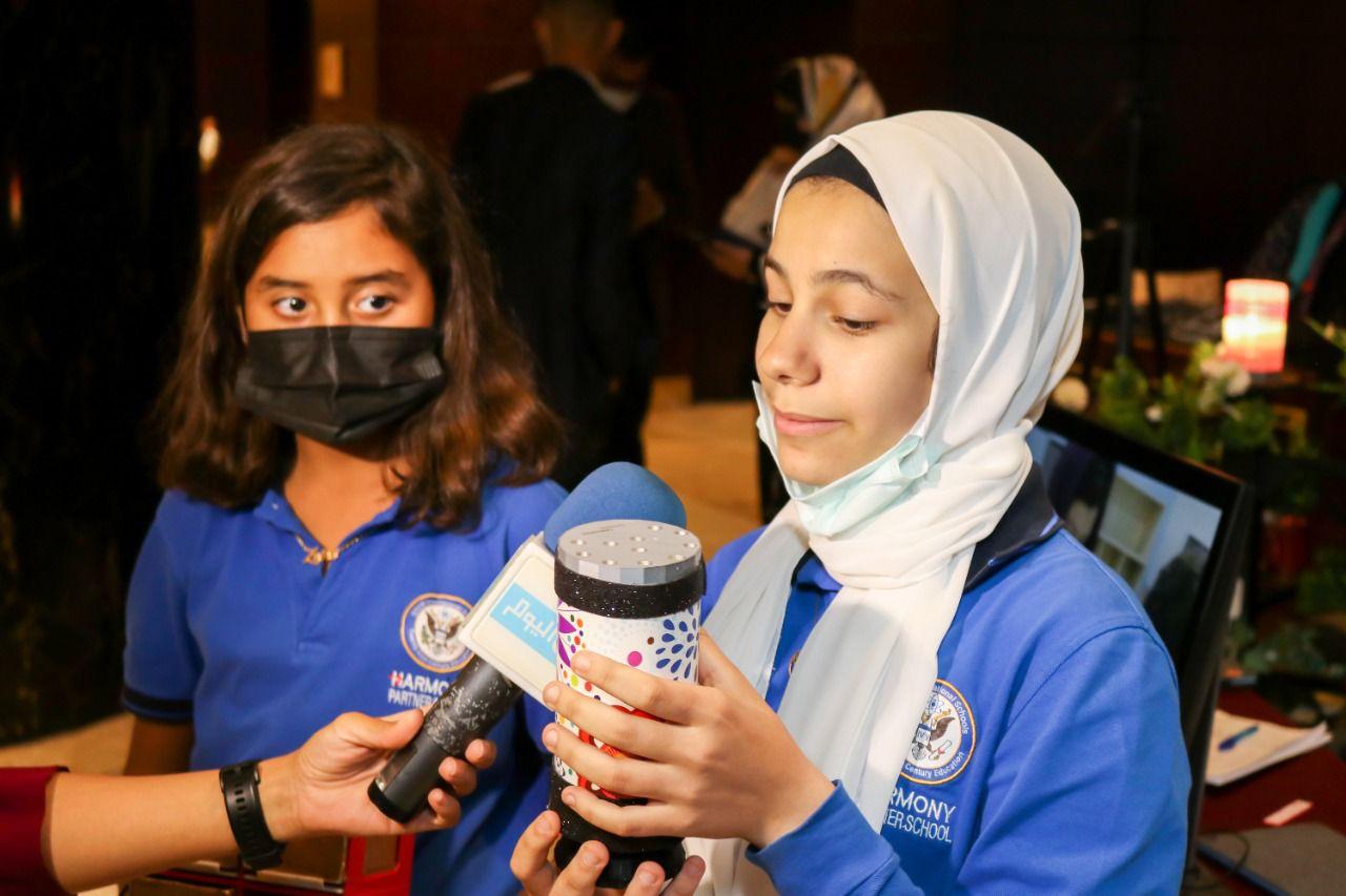 Students from IVY STEM International School participating in an educational event, with one student presenting and another holding a microphone. Technology and presentations are involved, as indicated by the computer monitor in the background.