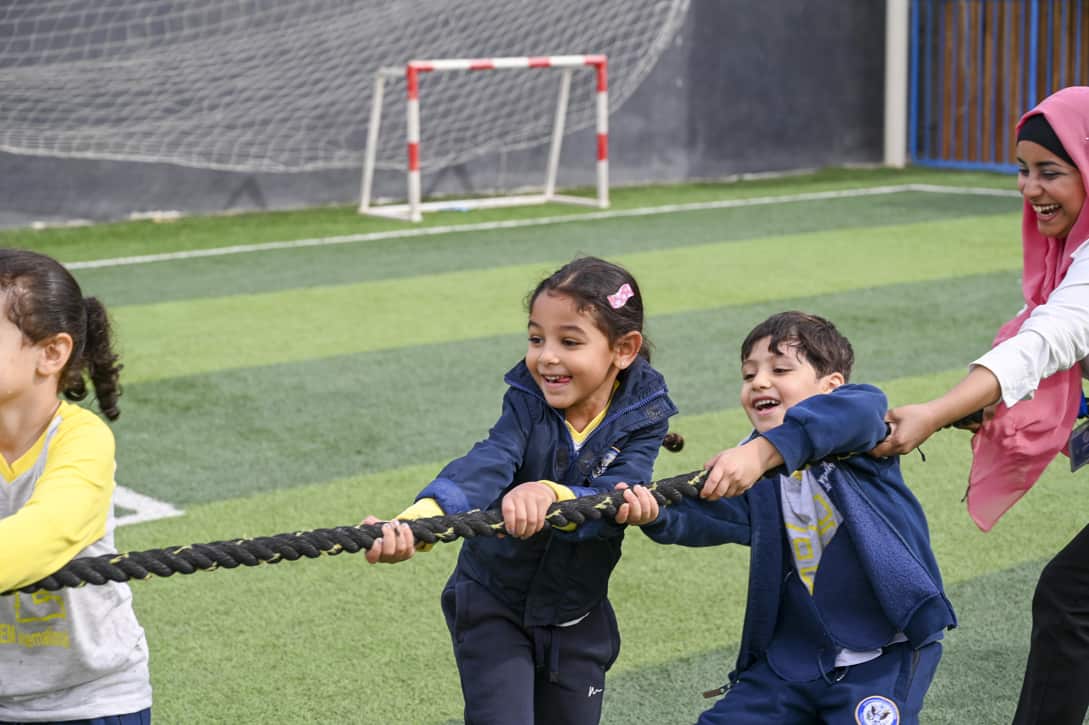 Children from IVY STEM International School participating in a fun tug-of-war activity on the school's sports field, with a teacher joining in the excitement.